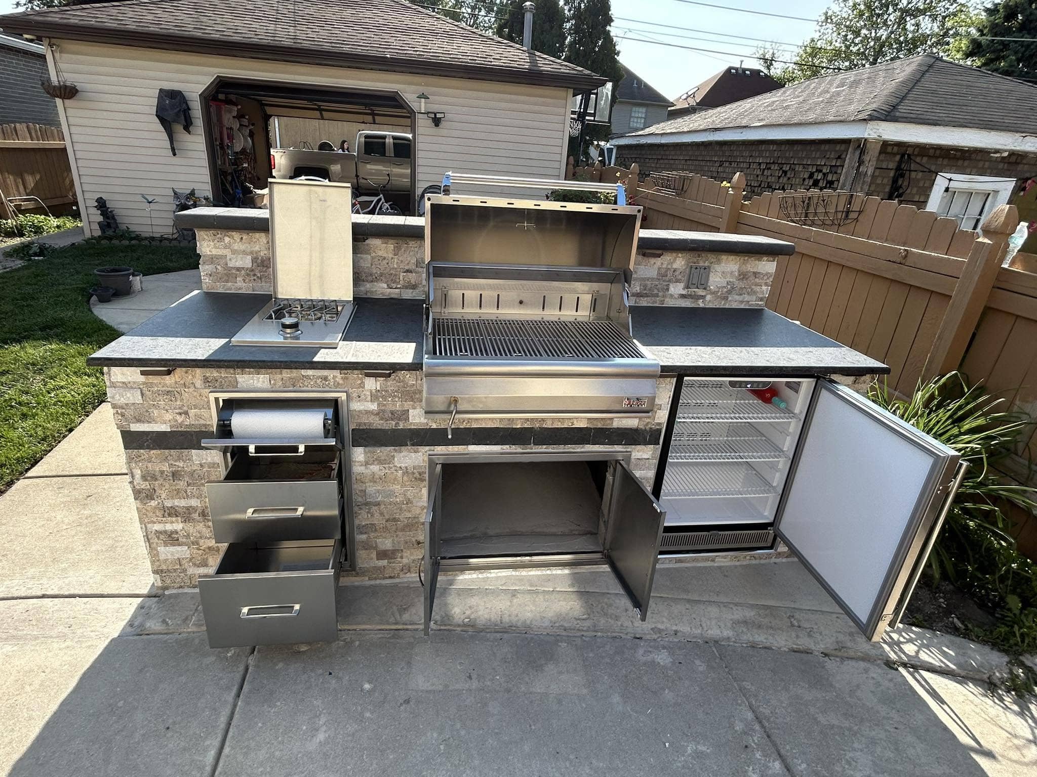 Outdoor kitchen with a stainless steel grill and a stone base on a backyard paver patio