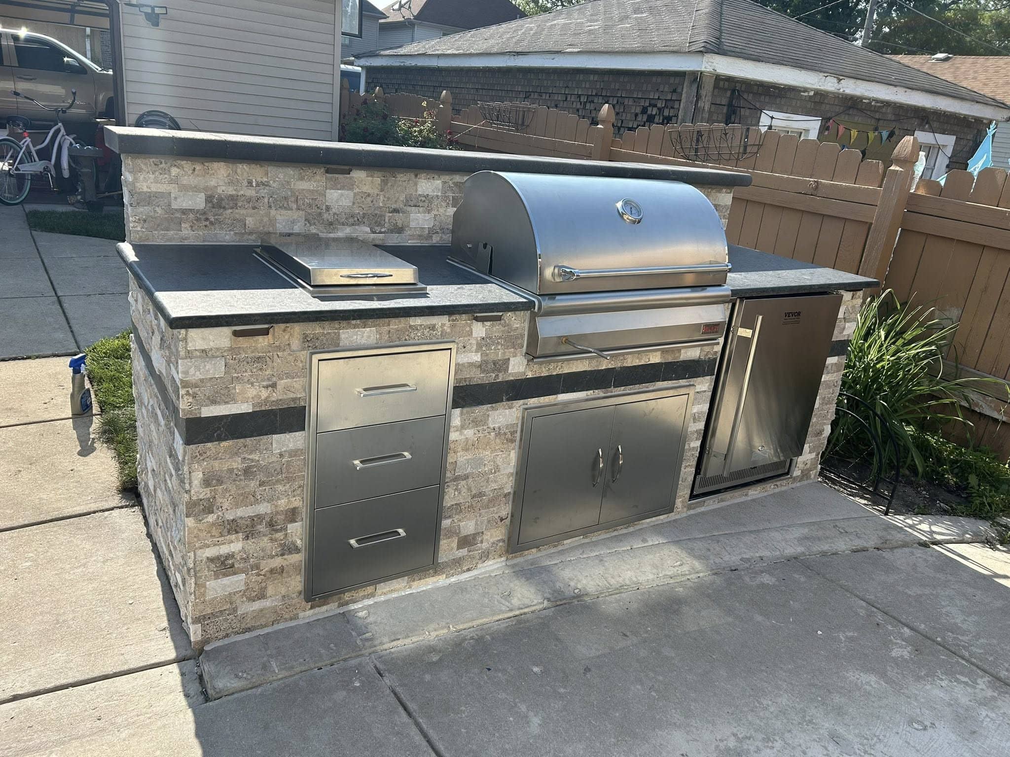 Stone outdoor kitchen with a stainless steel grill and hood and built-in cabinets on a paver patio